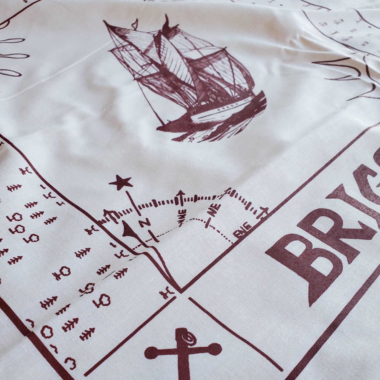 Close-up of a white fabric with brown nautical-themed designs including a ship, compass, and anchor.